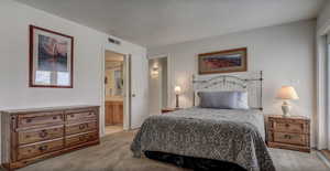 Bedroom featuring light colored carpet, a textured ceiling, and ensuite bath