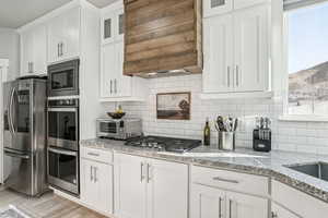 Kitchen with premium range hood, white cabinets, light wood-type flooring, backsplash, and stainless steel appliances