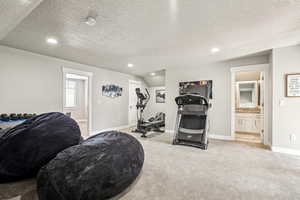 Exercise room featuring light colored carpet, a textured ceiling, and vaulted ceiling