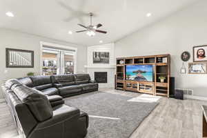 Living room featuring vaulted ceiling, ceiling fan, light hardwood / wood-style floors, and a fireplace