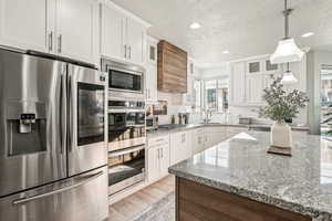 Kitchen with appliances with stainless steel finishes, a textured ceiling, white cabinets, pendant lighting, and backsplash