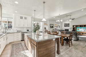 Kitchen featuring dishwasher, lofted ceiling, white cabinetry, hanging light fixtures, and light stone counters