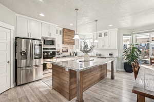 Kitchen with light stone countertops, a textured ceiling, a kitchen island, white cabinetry, and stainless steel appliances