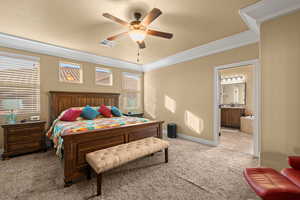 Bedroom featuring ceiling fan, connected bathroom, ornamental molding, and light carpet