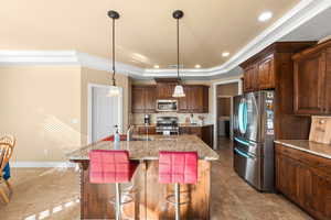 Kitchen with appliances with stainless steel finishes, decorative light fixtures, a raised ceiling, a kitchen island with sink, and a breakfast bar