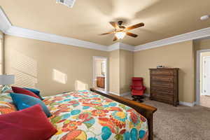 Bedroom with ceiling fan, connected bathroom, light carpet, and ornamental molding