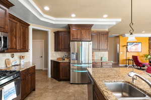 Kitchen with light stone countertops, pendant lighting, appliances with stainless steel finishes, decorative backsplash, and sink