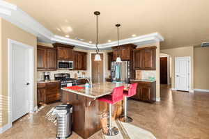 Kitchen with appliances with stainless steel finishes, hanging light fixtures, a kitchen island with sink, a breakfast bar, and light stone counters