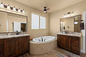 Bathroom with ceiling fan, a relaxing tiled tub, and vanity