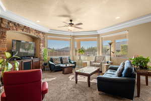 Living room with carpet flooring, a textured ceiling, a tray ceiling, and ceiling fan