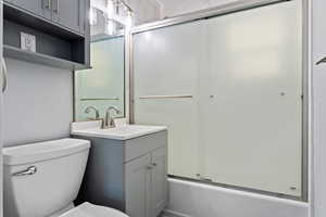 Full bathroom featuring enclosed tub / shower combo, vanity, and toilet