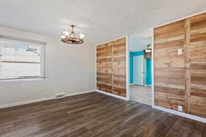 Unfurnished room with a textured ceiling, wood walls, ceiling fan with notable chandelier, and dark hardwood / wood-style floors