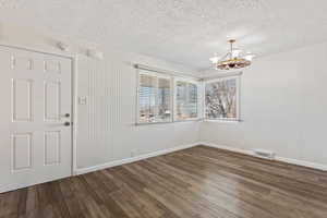 Unfurnished room featuring dark wood-type flooring and a notable chandelier