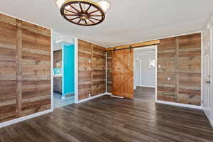 Empty room featuring dark wood-type flooring, a textured ceiling, a barn door, and wooden walls