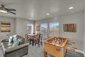 Recreation room featuring ceiling fan, light colored carpet, and a textured ceiling