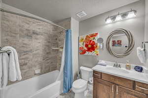 Full bathroom featuring a textured ceiling, toilet, vanity, and shower / bath combination with curtain