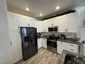 Kitchen featuring white cabinets, appliances with stainless steel finishes, dark stone counters, light hardwood / wood-style floors, and sink