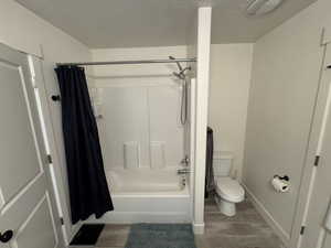 Bathroom with wood-type flooring, a textured ceiling, toilet, and shower / bath combo