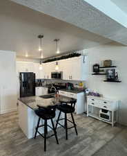 Kitchen featuring hanging light fixtures, a kitchen breakfast bar, white cabinets, sink, and stainless steel appliances