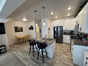 Kitchen with pendant lighting, sink, white cabinetry, an island with sink, and black refrigerator with ice dispenser