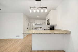 Kitchen featuring pendant lighting, white cabinets, appliances with stainless steel finishes, kitchen peninsula, and light wood-type flooring