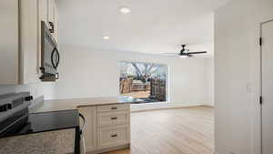 Kitchen featuring stainless steel electric stove, light hardwood / wood-style flooring, ceiling fan, white cabinetry, and light stone counters