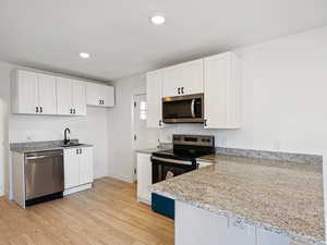 Kitchen with light stone counters, white cabinetry, light hardwood / wood-style flooring, and stainless steel appliances