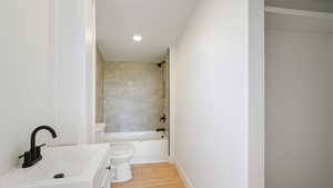 Full bathroom with hardwood / wood-style floors, toilet, vanity, and tiled shower / bath combo