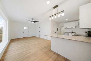 Kitchen with light stone countertops, dishwasher, decorative light fixtures, white cabinetry, and stove