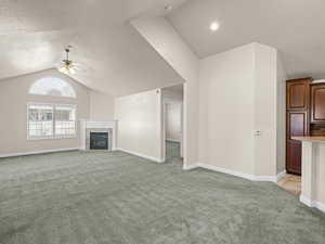 Unfurnished living room featuring a tiled fireplace, light colored carpet, vaulted ceiling, and ceiling fan