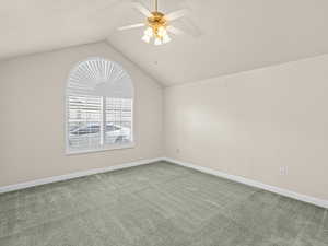 Carpeted spare room with ceiling fan and vaulted ceiling