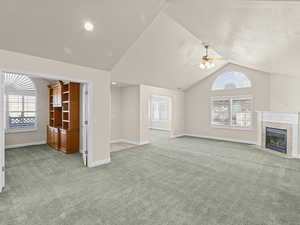 Unfurnished living room featuring ceiling fan, light carpet, a tiled fireplace, and vaulted ceiling