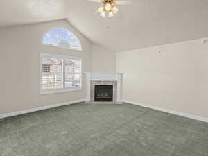 Unfurnished living room with a textured ceiling, lofted ceiling, carpet flooring, ceiling fan, and a tiled fireplace