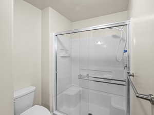 Bathroom featuring toilet, a textured ceiling, and a shower with shower door