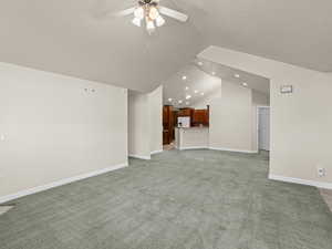 Unfurnished living room featuring ceiling fan, carpet, and lofted ceiling