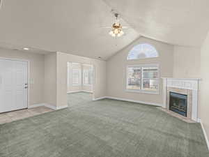 Unfurnished living room with ceiling fan, a textured ceiling, a tile fireplace, light carpet, and vaulted ceiling