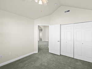 Unfurnished bedroom featuring lofted ceiling, dark colored carpet, a closet, and ceiling fan