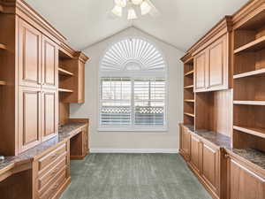 Unfurnished office featuring ceiling fan, lofted ceiling, dark carpet, and built in desk