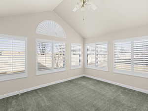 Carpeted spare room with plenty of natural light, high vaulted ceiling, and ceiling fan