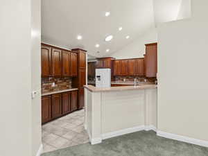 Kitchen featuring vaulted ceiling, white refrigerator with ice dispenser, decorative backsplash, kitchen peninsula, and light tile patterned flooring