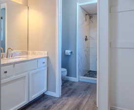 Bathroom with tiled shower, vanity, toilet, and hardwood / wood-style floors