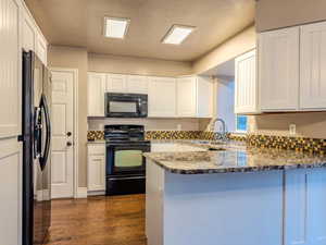 Kitchen with dark stone countertops, kitchen peninsula, sink, and black appliances