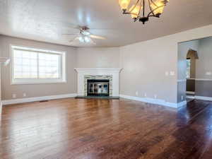 Unfurnished living room with a stone fireplace, wood-type flooring, a textured ceiling, and ceiling fan with notable chandelier