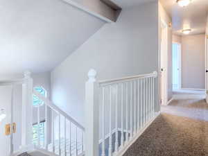 Corridor with carpet floors and vaulted ceiling with beams