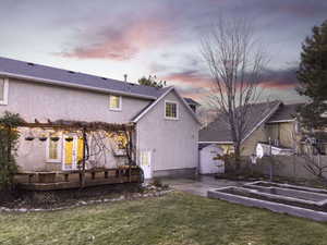 Back house at dusk with a storage shed, a wooden deck, and a lawn