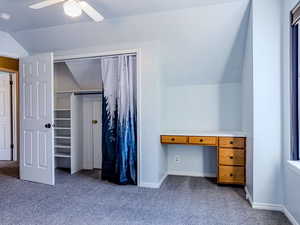 Unfurnished bedroom with lofted ceiling, carpet floors, built in desk, and ceiling fan