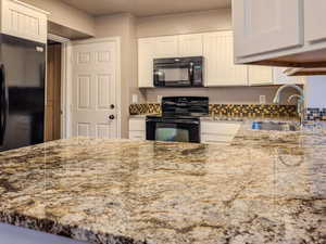 Kitchen with black appliances, sink, white cabinets, light stone counters, and kitchen peninsula