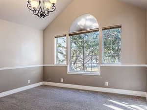 Empty room featuring lofted ceiling, a chandelier, and carpet