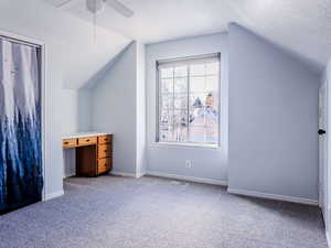 Additional living space with ceiling fan, vaulted ceiling, carpet, and a textured ceiling