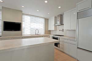 Kitchen featuring built in refrigerator, wall chimney exhaust hood, white cabinetry, sink, and wall oven